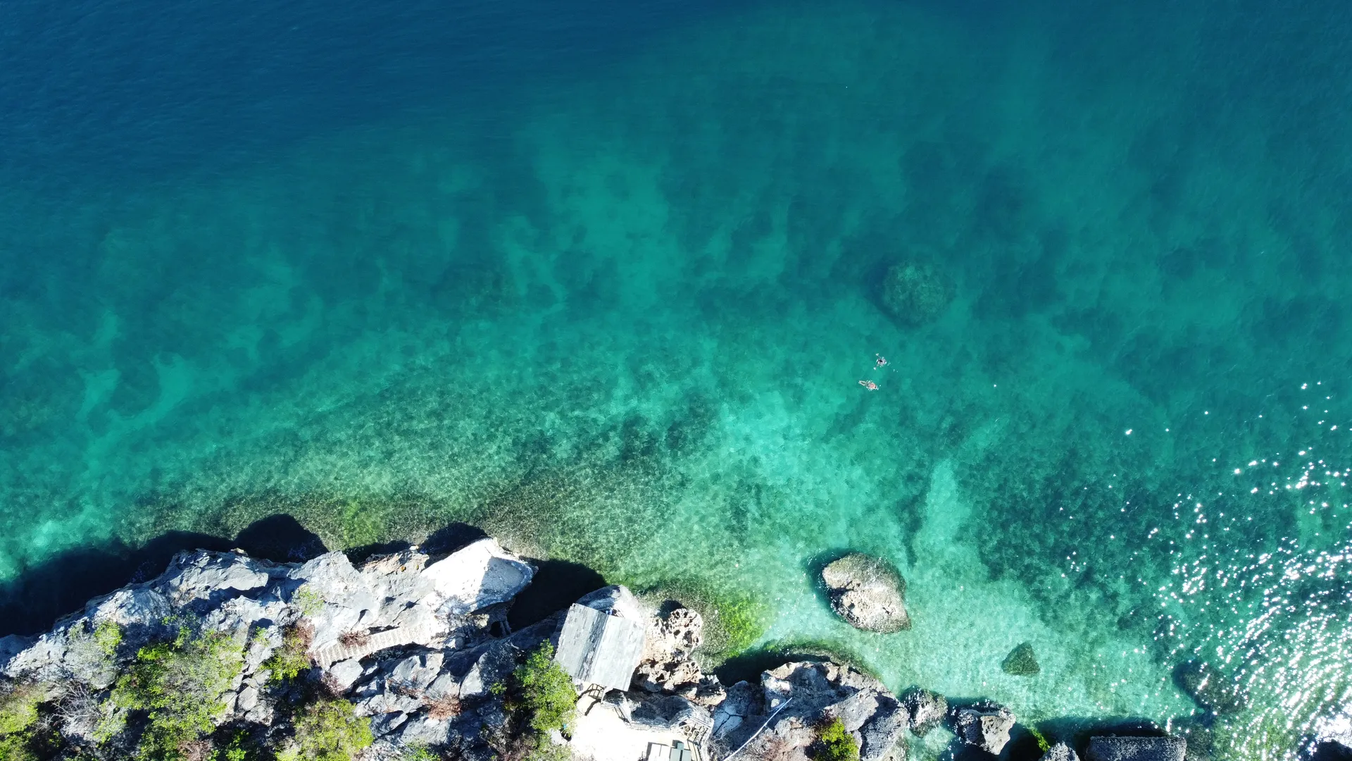 Clear turquoise shallows over white sand meeting a rocky limestone shore